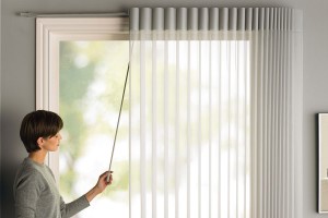 Woman adjusting white vertical blinds tree in background out of focus